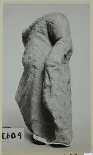 Headless draped stone figure from Mersinaki, photographed against a plain grey backdrop.