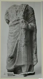 Headless draped standing figure in limestone from Mersinaki, photographed against a grey backdrop.
