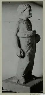 Standing limestone statue of a draped figure from Mersinaki, shown in profile on a wooden base.