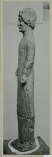 Limestone statue of a standing female figure, shown in profile facing left.