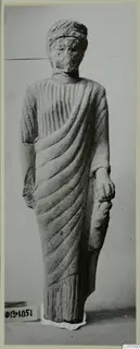 Limestone statue of a standing draped figure from Mersinaki, face worn and features indistinct.