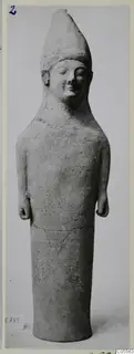 Tall terracotta standing figure with a conical headdress, shown upright against a plain grey background