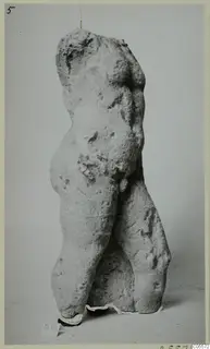Headless, armless torso of a standing figure in pale stone, from Mersinaki, photographed against a grey backdrop