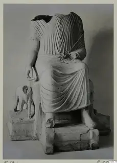 Terracotta statuette of a seated, headless draped figure with a small animal figure on its base.