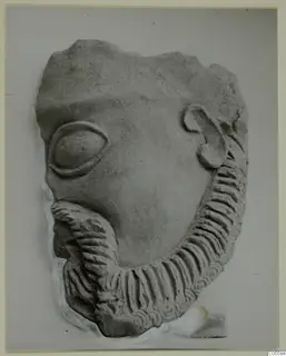 Fragment of a carved face from Mersinaki, with an almond-shaped eye, a curled ear and a ridged beard