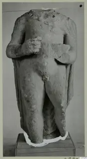 Headless standing male statue in limestone from Mersinaki, shown frontally on a wooden box base