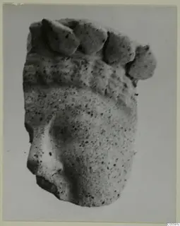 Fragment of a pitted sculpted figure, possibly a head, with a row of rounded forms along its upper edge
