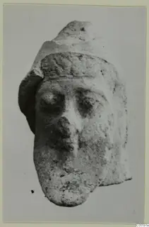 Terracotta head fragment with large eyes, a prominent nose and a band across the brow, shown against a plain background