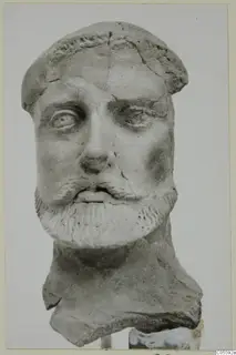 Sculpted head of a bearded man in grey terracotta or limestone, shown from the front, with cracks across the face.