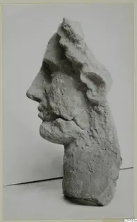 Carved stone head fragment in profile, facing left, with the top and back broken away