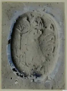 Oval engraved seal or gem with incised lines and a branching motif, photographed on a grey card
