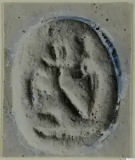 Oval seal or gem with a carved design, photographed on a cracked, damaged mount