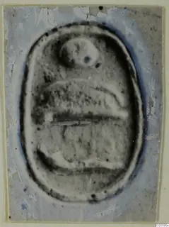 Oval seal or gem with a carved design, a rounded form near the top, shown on a damaged blue-grey mount.