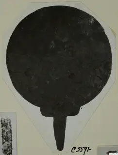 Plate from Marion: a dark round disc with a narrow tang extending downward, shown on a white card mount