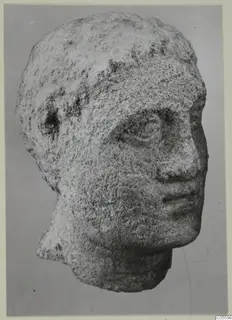 Limestone head statue from Mersinaki, shown in three-quarter view against a grey backdrop.