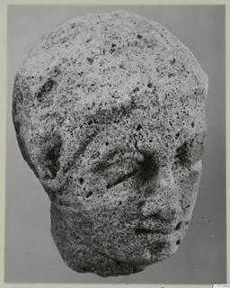 Limestone sculpture head from Mersinaki, face partly worn, photographed against a plain grey background