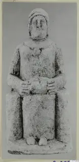Seated limestone figure with hands clasped in its lap and a close-fitting head covering