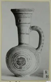 White Painted IV juglet with a flared neck, a strap handle and concentric circles painted on the body.