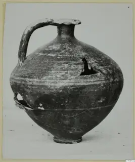 Jug with a tall strap handle, narrow neck and rounded body, with a broken hole in the shoulder and a chipped base