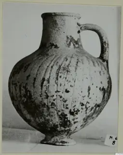 Pottery Black Slip jug with a single loop handle and vertical grooves on its rounded body