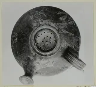 Oil lamp seen from above, with a central filling hole, a ribbed handle on the right and dark painted decoration