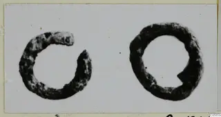 Two dark, corroded rings shown side by side on a pale card: the left one open, the right one closed.