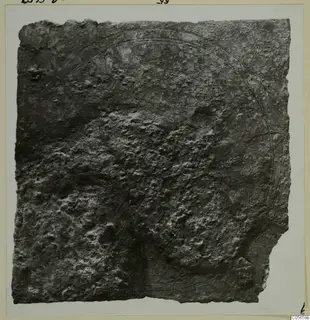 Corroded bronze fragment from Marion Tomb 60, mounted on a card, with a faint curved line incised across its surface