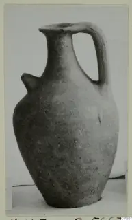 Jug with a tall neck, a strap handle and a small projecting lug on the shoulder, photographed against a pale background