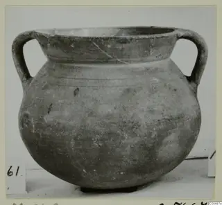 Two-handled vessel with a wide mouth and rounded body, photographed on a light surface with a number label beside it
