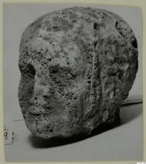 Weathered limestone head fragment from Mersinaki, showing a worn face on its left side with nose and mouth visible