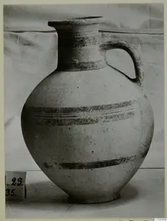 Pottery White Painted IV jug with a single loop handle and dark painted bands, standing on a surface beside a number label.