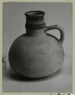 Round jug with a ribbed neck and a strap handle, photographed on a plain grey background. Find from Amathus, tombs 10–26.