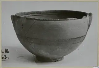 Pottery Black-on-Red bowl with two small handles and dark painted bands on its body, seen from the side.