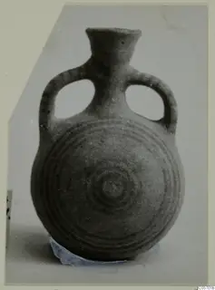 Pottery bottle with two loop handles and concentric circles on the body, photographed on a grey card mount