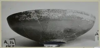 Pottery Red Slip bowl, a shallow bowl with a ring foot, cracked and mended, shown on a dark stand