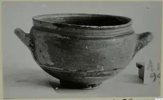 Pottery bowl with two horizontal handles and a wide rim, photographed on a pale surface, from Amathus tombs