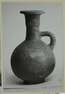 Red-slipped pottery juglet with a single handle, a flat rim and a rounded body, photographed on a plain background.