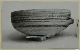 Pottery White Painted IV bowl from Amathus with horizontal dark bands and one side handle, standing on a small stone support.