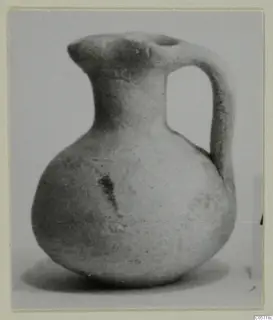 Plain white pottery juglet with a round body, short neck and loop handle, shown against a pale background.