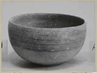 Rounded pottery bowl with horizontal banding, photographed on a plain pale surface