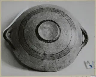 Pottery bowl with two loop handles and concentric dark bands, seen from above against a pale background