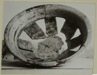 Broken pottery plate-jug seen from above, its rim ring surrounding several missing and displaced wall fragments.