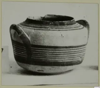 Round-bodied pottery jug with two loop handles and horizontal dark bands, photographed on a plain surface.