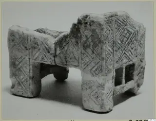 Stone object from Marion with incised lozenge and chevron patterns, standing on four rounded supports.
