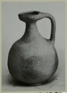 Small pottery jug with a single loop handle and a trefoil-like spout, photographed on a plain surface.