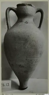 Tall two-handled plain pottery amphora with a chipped rim, standing on a pale surface against a grey backdrop.
