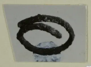 Dark coiled metal object from Stylli, a spiral of about two turns resting on a pale blue stone support.