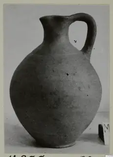 Pottery jug with a single loop handle and narrow neck, photographed against a plain background.