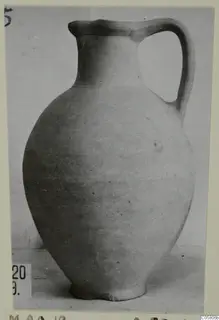 Plain white-slipped pottery jug with a single loop handle, shown against a plain backdrop.