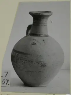 Pottery Bichrome III jug with a flared neck, one handle and painted bands, photographed on a plain surface
